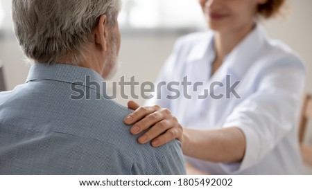 Close up young woman doctor touching senior patient shoulder at meeting in hospital, caring physician gp comforting and supporting mature man at medical appointment, psychological help concept