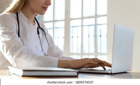 Close Up Young Woman Doctor Wearing Uniform Working On Laptop In Hospital Office, Sitting At Desk In Hospital, Therapist Physician Nurse Typing, Using Medical Apps, Consulting Online