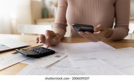Close up young woman doing financial paperwork, planning investments, calculating domestic expenditures taxes utility bills, checking data in mobile e-banking application or paying for service online.
