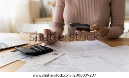 Close up young woman doing financial paperwork, planning investments, calculating domestic expenditures taxes utility bills, checking data in mobile e-banking application or paying for service online.