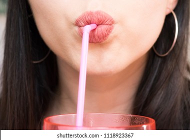 Close up of young woman drinking from pink cup with a straw 