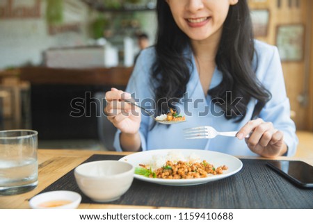 Close up of young woman eating thai food in restaurant. Young woman eats pork with rice and vegetables at restaurant. 
