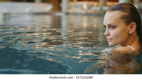 Close Up Of An Young Woman Is Enjoying And Having Relax In An Indoor Illuminated With Night Lights Swimming Pool In A Luxury Wellness Center.