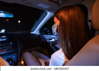 Close up of young woman, female passenger wearing protective mask while sitting in front seat of the car. Couple watching a movie at drive in cinema. Transportation, safety concept. Rear view
