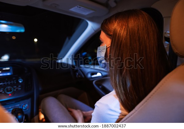 Close up of young woman, female passenger wearing\
protective mask while sitting in front seat of the car. Couple\
watching a movie at drive in cinema. Transportation, safety\
concept. Rear view