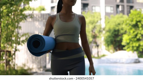 close up Young woman hand hold Yoga mat for daily yoga exercise at poolside of the condominium - Powered by Shutterstock