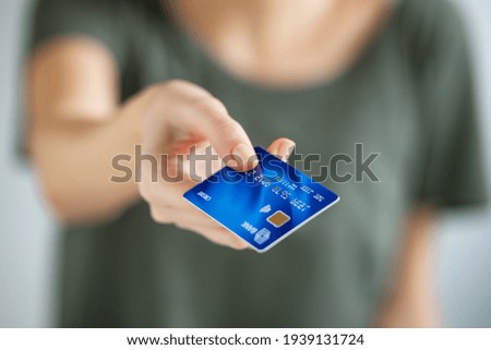 Close up of young woman hand holding credit card. Woman extending hand to give credit card to cashier. Close up of a girl paying with blue creditcard.