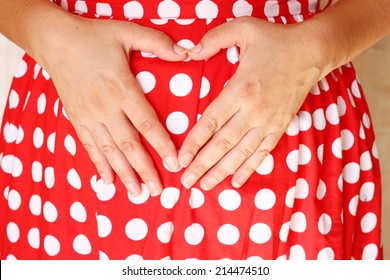 Close Up Of Young Woman Hands On Tummy Creating Heart Shape Wearing Red Dress.