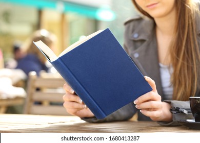 Close up of young woman hands reading a hard cover blue book on a cafe terrace
