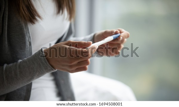 Close up of young woman hold in hands positive or\
negative pregnancy test thinking pondering, millennial female\
expecting baby undergo fertility infertility treatment, IVF, future\
maternity concept