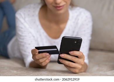 Close up young woman holding cellphone and bank credit plastic card in hands, entering payment information, purchasing goods in internet store or paying for services, online shopping concept.