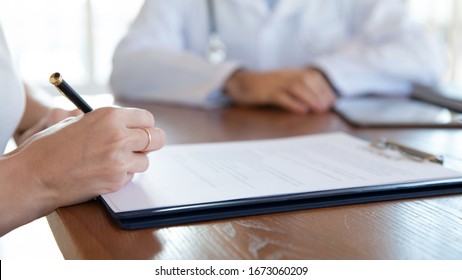 Close up young woman holding pen, ready to sign medical insurance contract with family doctor. Female patient putting signature on agreement with physician during meeting in clinic hospital.