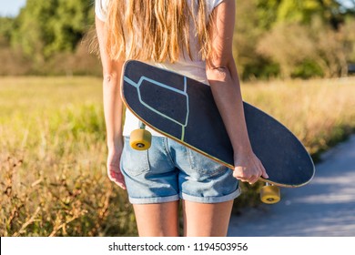 Close Up Of Young Woman Holding Skateboard Deck In Hands On A Summer Day