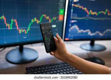 Close Up Of A Young Woman Holding A Smartphone And Checking The Stock Market Online. Businesswoman Working And Trading Stocks 