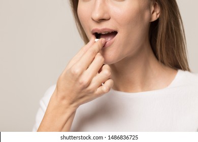 Close Up Of Young Woman Isolated On Grey Background Take Medicine Antidepressant Or Birth Control Pill, Female Put Tablet In Mouth Have Painkiller Or Antibiotic. Healthy Lifestyle, Medication Concept