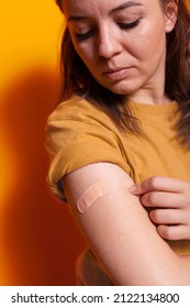 Close Up Of Young Woman Looking At Adhesive Bandaid On Arm, After Receiving Vaccine Against Coronavirus. Person Having Medical Bandage On Hand For Protection. Vaccinated Adult With Patch