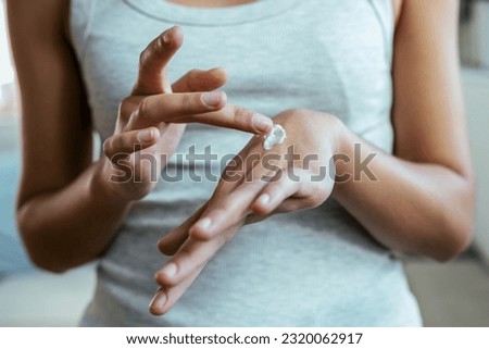 Close up of young woman putting cream on her hands at home