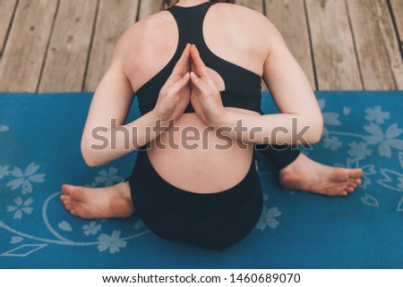 Close up of young woman sitting in asana yoga pose. Legs crossed. Hands in praying position behind back. Sitting on blue mat alone