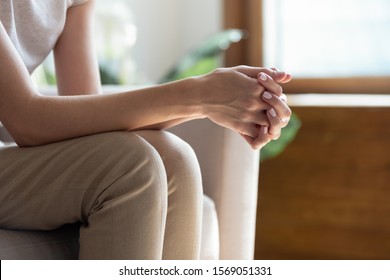 Close up young woman sitting on sofa with folded hands on knees. Thoughtful millennial lady waiting for important news, feeling puzzled, making complicated decision or recollecting memories at home. - Shutterstock ID 1569051331