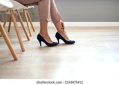 Close up young woman sitting on chair, taking off high heel shoes, massaging tired foot relieving pain ache in office. Exhausted millennial lady feeling feet discomfort, wearing narrow footwear.