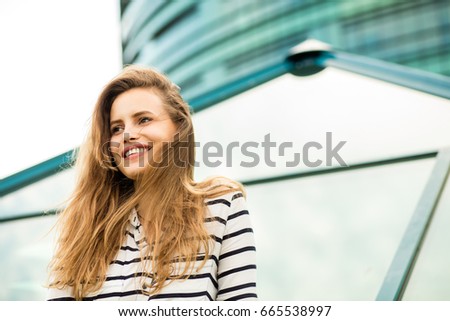 close up of a young woman in stripes standing outside, with business center behind