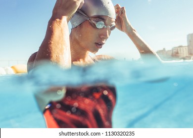 Close up of young woman swimmer inside the pool adjusting her goggles. Professional swimmer taking a break while training in outdoor pool.