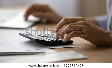 Close up young woman using calculator, managing household monthly budget, summarizing taxes or bills, planning future investments, doing financial affairs at home, accounting bookkeeping concept.