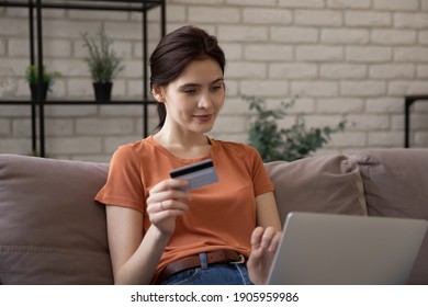 Close up young woman using laptop, holding plastic credit or debit card, paying online, attractive female looking at computer screen, buying, customer making internet payment, sitting on couch