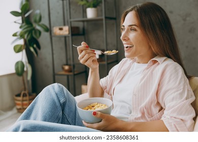 Close up young woman wear casual clothes sit in armchair eat breakfast muesli cereals with milk fruit in bowl stay home hotel flat rest relax spend free spare time in living room indoor Lounge concept - Powered by Shutterstock