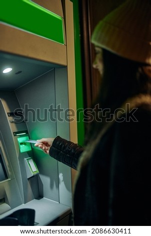 Close up of young woman with woolen cap inserting her bank card in a cash machine