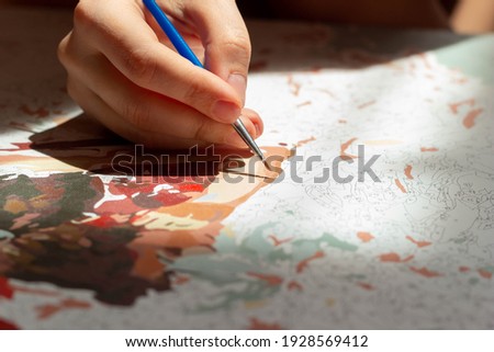 Close up of a young woman's artist hand paintting a picture by numbers. Sunny day. Creativity and art relieve stress. Hobby at home