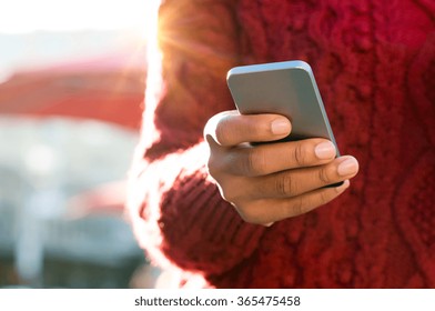Close Up Of A Young Woman's Hand Typing Text Message On Her Smartphone. African Young Woman Is Typing On Touch Screen Mobile Phone. Close Up Of Female Hand Texting A Message Phone Outdoor. 
