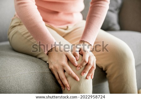 Close up of young women sitting on sofa and holding painful knee, female suffering chronic tendon arthritis, Health Care and Medical Concept. 