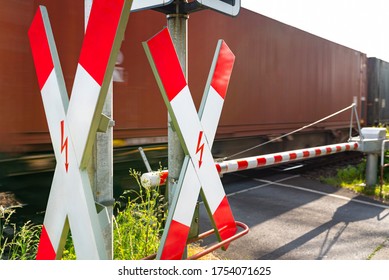 Closed Barrier At The Railway Crossing With St. Andrew Cross, Visible Blurred Red Wagon In Motion.