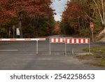 Closed barriers at the entrance gate of a parking lot at the end of a road. Autumn colors