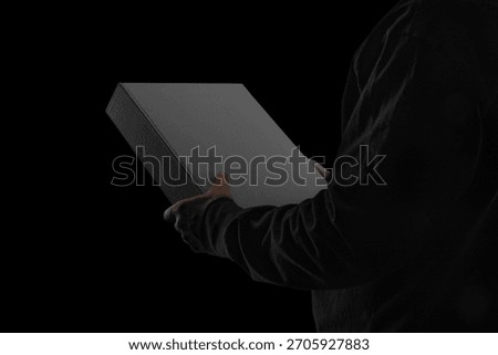 A closed binder box held by a person wearing dark clothing. Minimalistic blackout style with moody, low-key lighting. Perfect for showcasing packaging, premium stationery, branding concepts