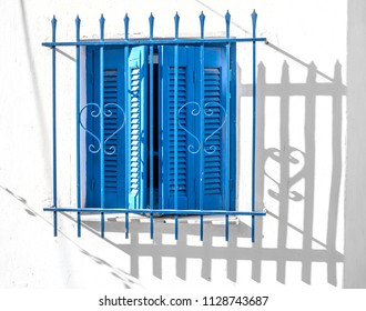 Closed Blue Wooden Window Shutters With Wrought Security Grate On White Wall In Greece