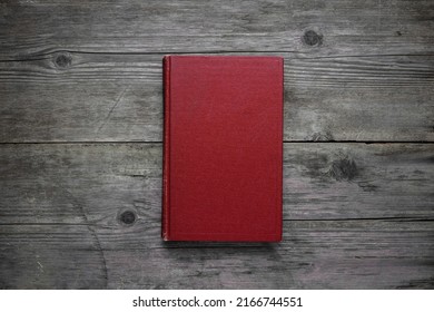 A Closed Book On An Old Wooden Table. Red Hard Cover. Vintage Background.