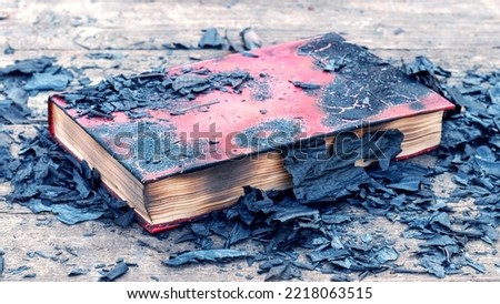 A closed burnt book among the ashes and charred book pages