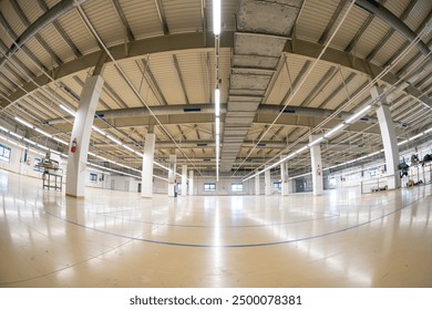 Closed down empty factory interior manufacturing hall with tall ceiling, concrete beams. Wide angle shot, ceiling mounted neon lights, no people.