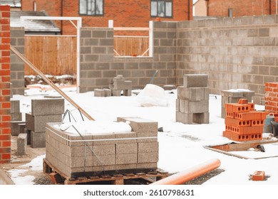 Closed empty construction site in winter shows gray concrete blocks stacked amidst snow-covered ground with unfinished walls
