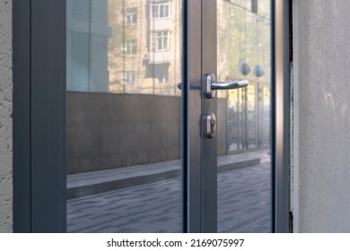 Closed Entrance Glass Door With Buildings Reflection And Some Water Drop Spots. Metal Handle And Lock. Selective Focus.