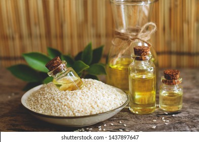 Closed Up Extract Sesame Oil In White Sesame Seed In Ceramic Dish Put Together With Another Three Glass Bottles Over Green Leaf Background In Dark Tone And Soft Light Filter