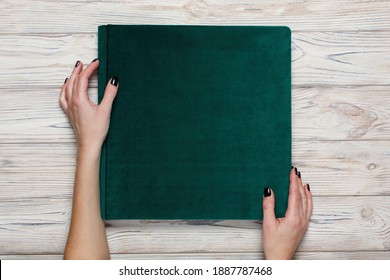 Closed Green Wedding Photo Album Isolated On Wooden Background.
Person Opens A Photobook.
Womans Fingers Touch A Bright Family Photoalbum. Womans Hand Holding Family Photo Album With Beautiful Pattern