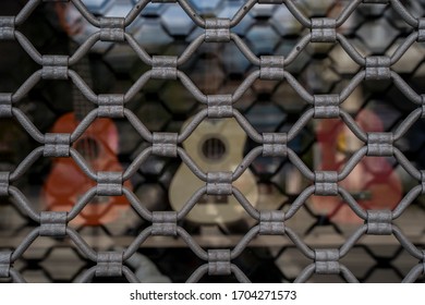 Closed Guitar Shop Window, With Several Instruments Displayed Behind The Security Bars