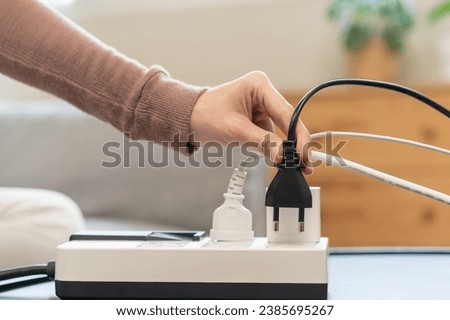 Closed up hand of woman plugged in, unplugged electricity cord cable on socket on table for energy saving, electric power on plate outlet, control expense electrical appliances, environment concept.