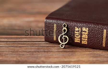 Closed Holy Bible Book with rustic old treble clef note on wooden background. God Jesus Christ is My Song and Salvation. Christian biblical concept of praise, worship, joy in the LORD. A close-up.