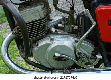 closed iron engine box with crank and gear shifter and part of the exhaust pipe in an old motorcycle on the street during the day