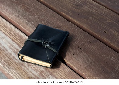 A Closed Leather Bound Black Journal Outdoors On Table, Wrapped With Cord  With Copy Space.