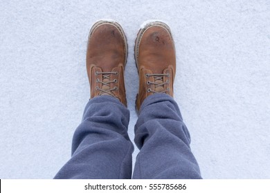 Closed Men's Legs In Work Shoes And Gray Sweatpants, Snow On Background, First Person Perspective